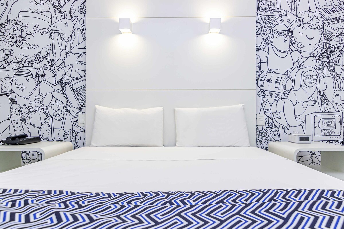A bedroom with a bed, two bedside tables, a nightstand, and a wall with a black and white pattern.
