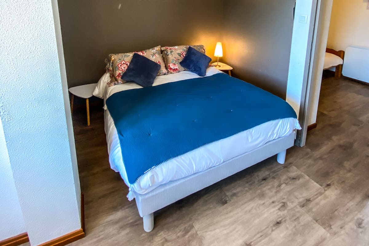 A bedroom with a bed, a nightstand, a wall-mounted lamp, and a painting.