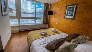 Habitación de hotel con un ventanal que ofrece vistas a un paisaje nevado y una pared de madera con un cartel enmarcado.