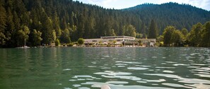 Un hotel junto al lago, con un edificio grande, rodeado de árboles y una colina boscosa al fondo.