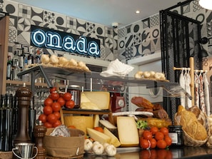 A cheese and charcuterie display with various cheeses, tomatoes, garlic, and bread. - ibis Styles Barcelona City Bogatell (Barcelona)