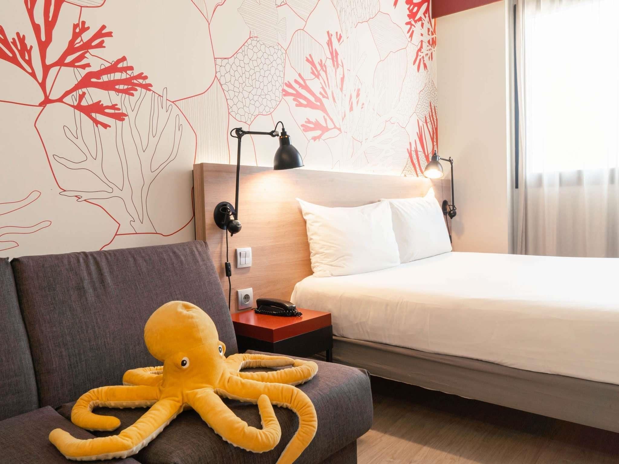 Een hotelkamer met een bed, een bank, een nachtkastje, een lamp en decoratieve wanddecoratie.