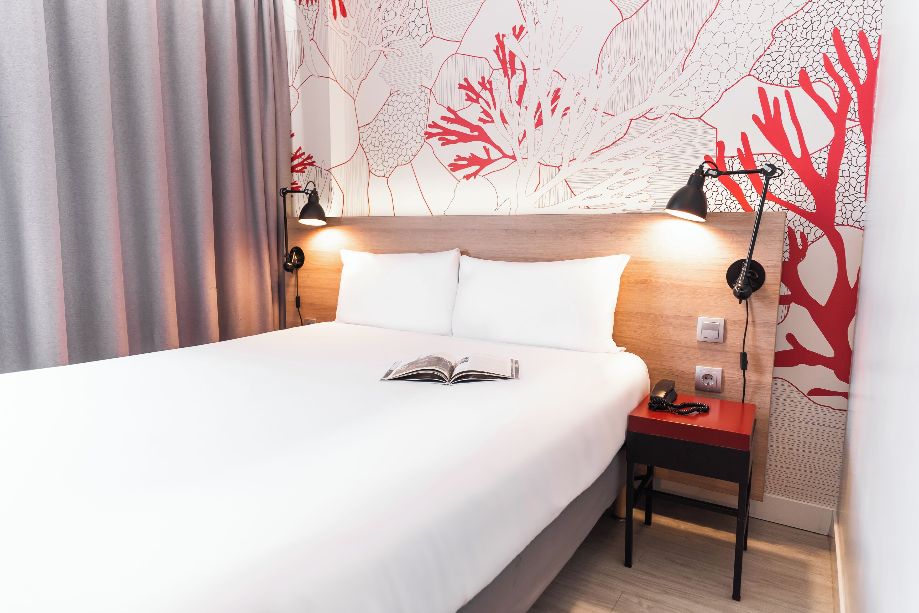 Una cama bien hecha con sábanas blancas, una mesita de noche con lámpara y una pared con un mural de arrecife de coral.
