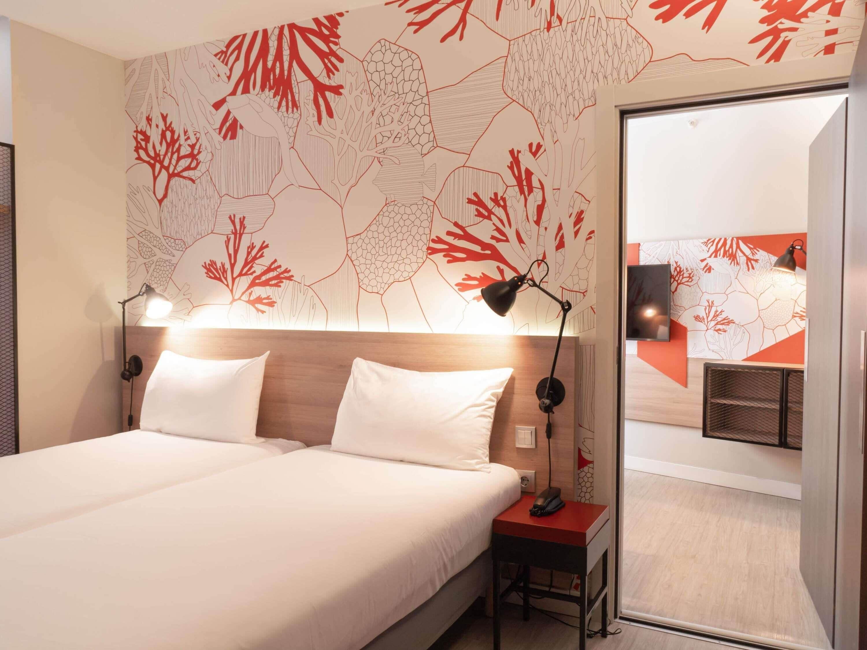 A hotel room with a bed, bedside lamps, a nightstand, and a wall with a coral reef pattern.