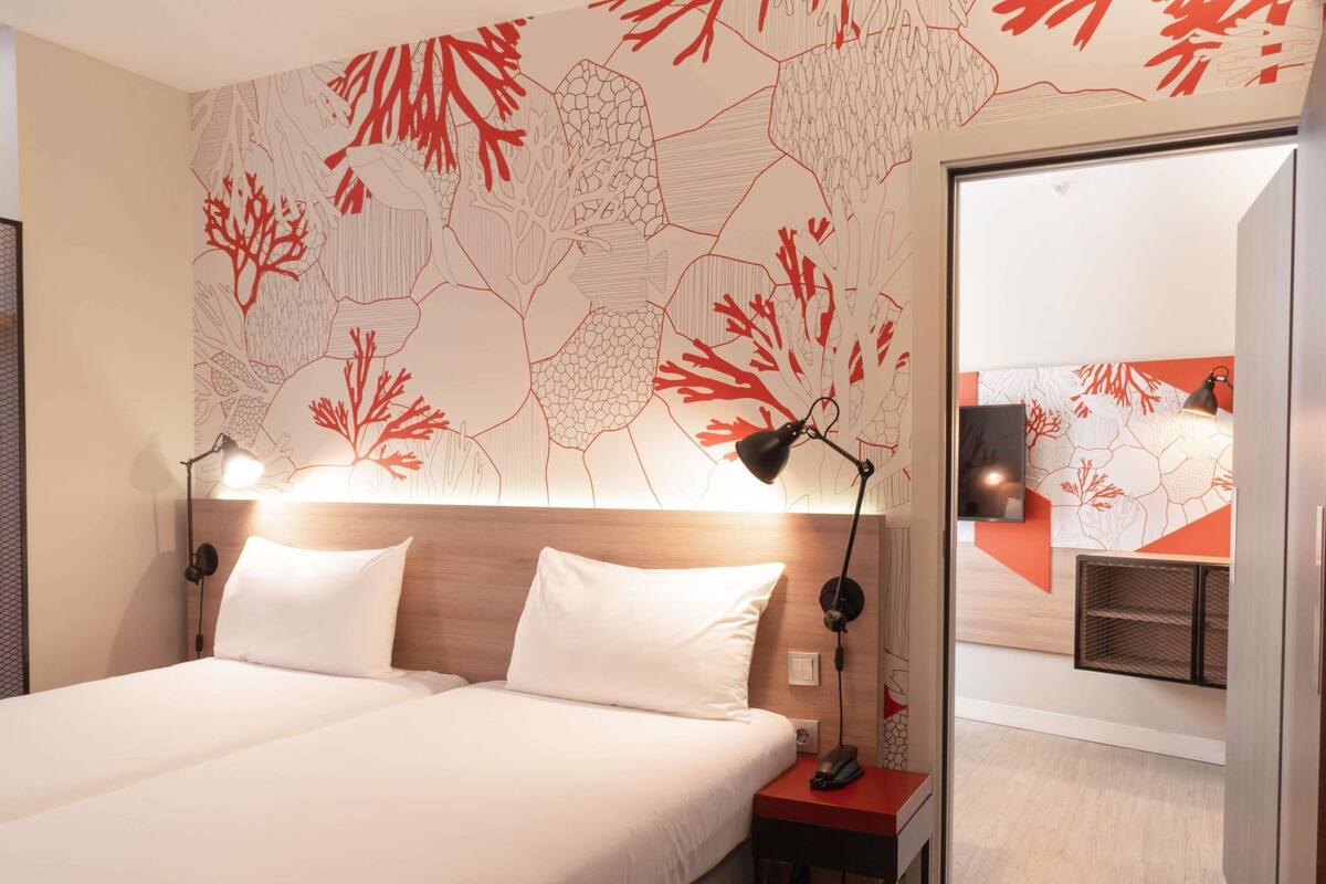 Habitación de hotel con cama, lámparas de noche, mesita de noche y una pared decorada con un diseño de arrecife de coral.