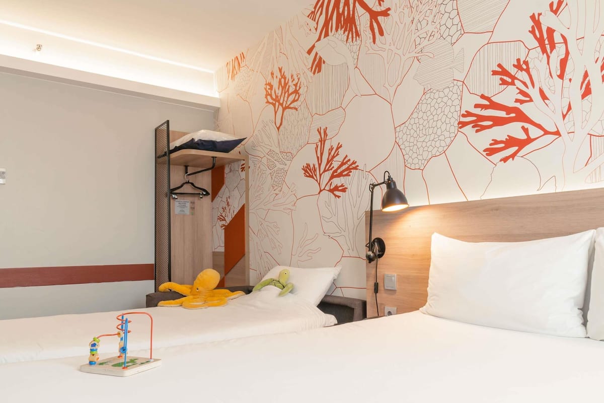 A hotel room with two beds, a wooden headboard, a wall mural, a hanging lamp, and a small toy.