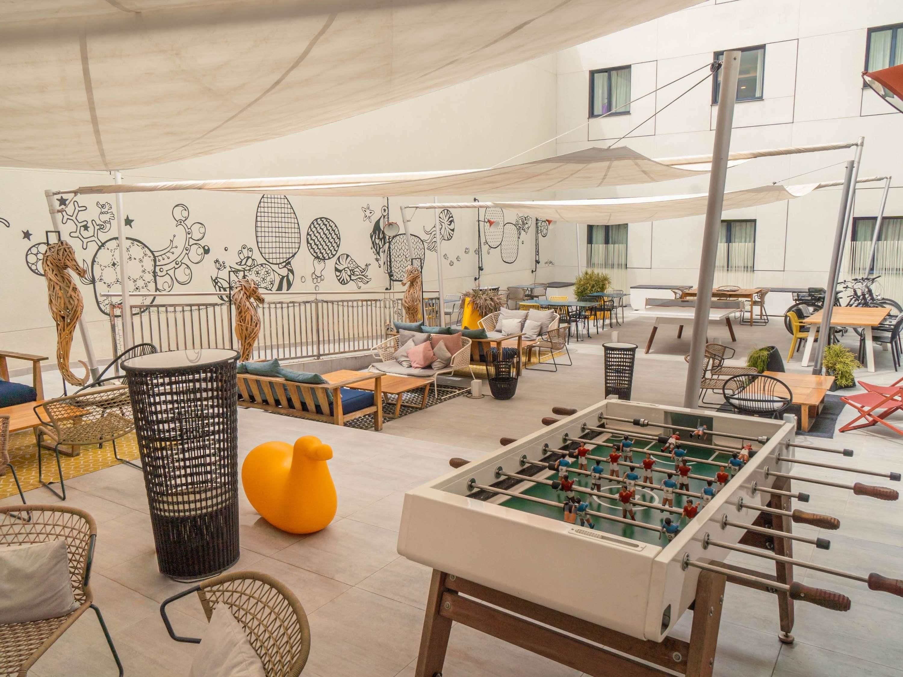 Un amplio espacio al aire libre con mesas, sillas y una mesa de futbolín.