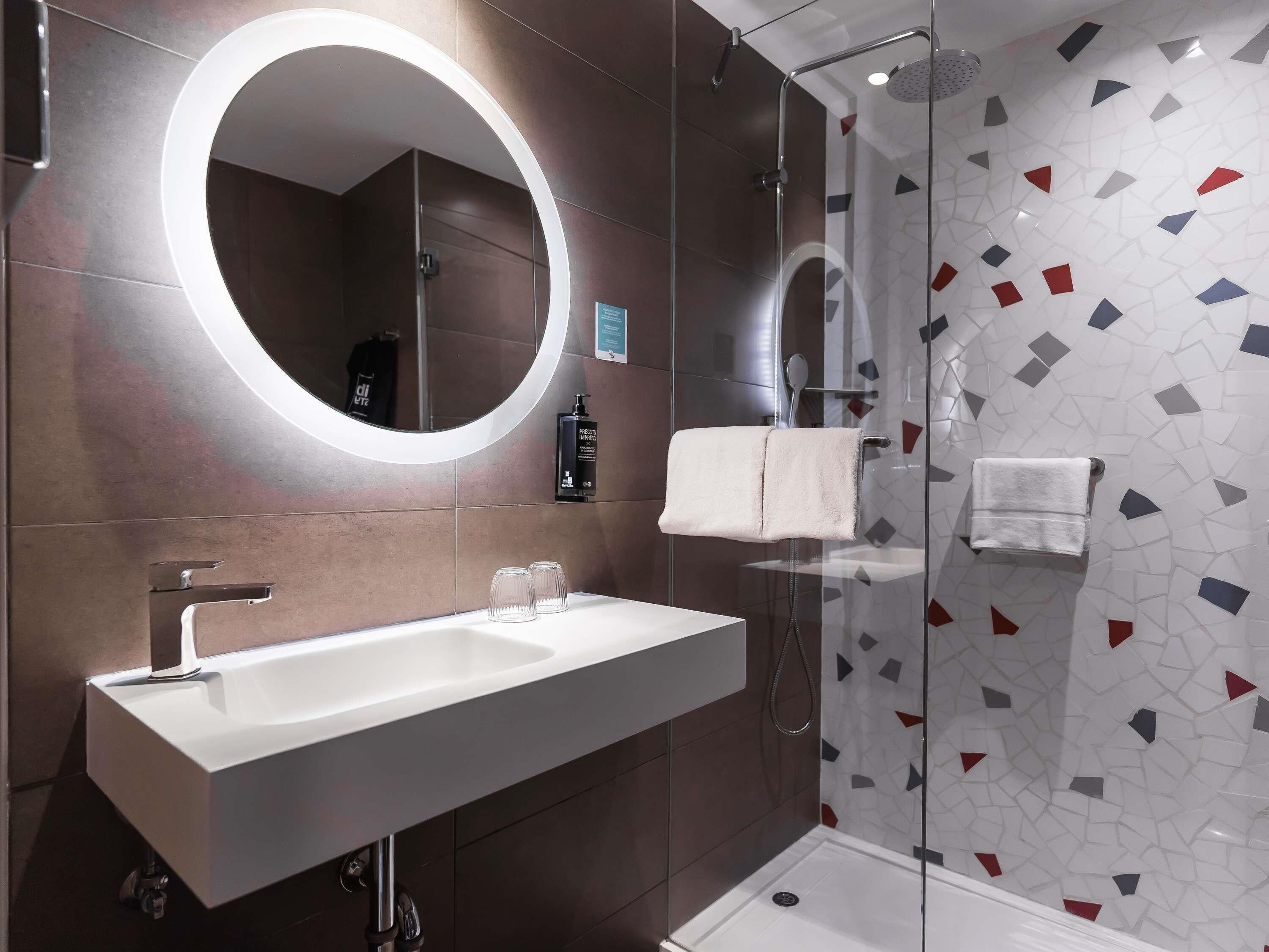 A modern bathroom with a large mirror, a white sink, and a glass shower enclosure.