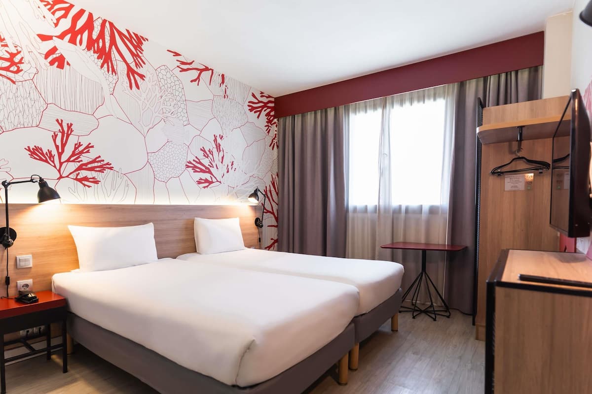 A hotel room with a large bed, a desk, a mirror, and a wall with a red and white abstract design.