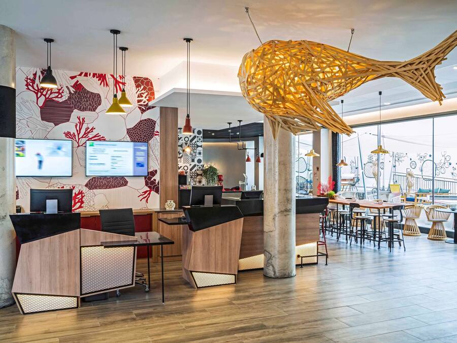 Un hall d’hôtel moderne doté d’un comptoir d’accueil, d’ordinateurs et d’un grand luminaire suspendu au design original.