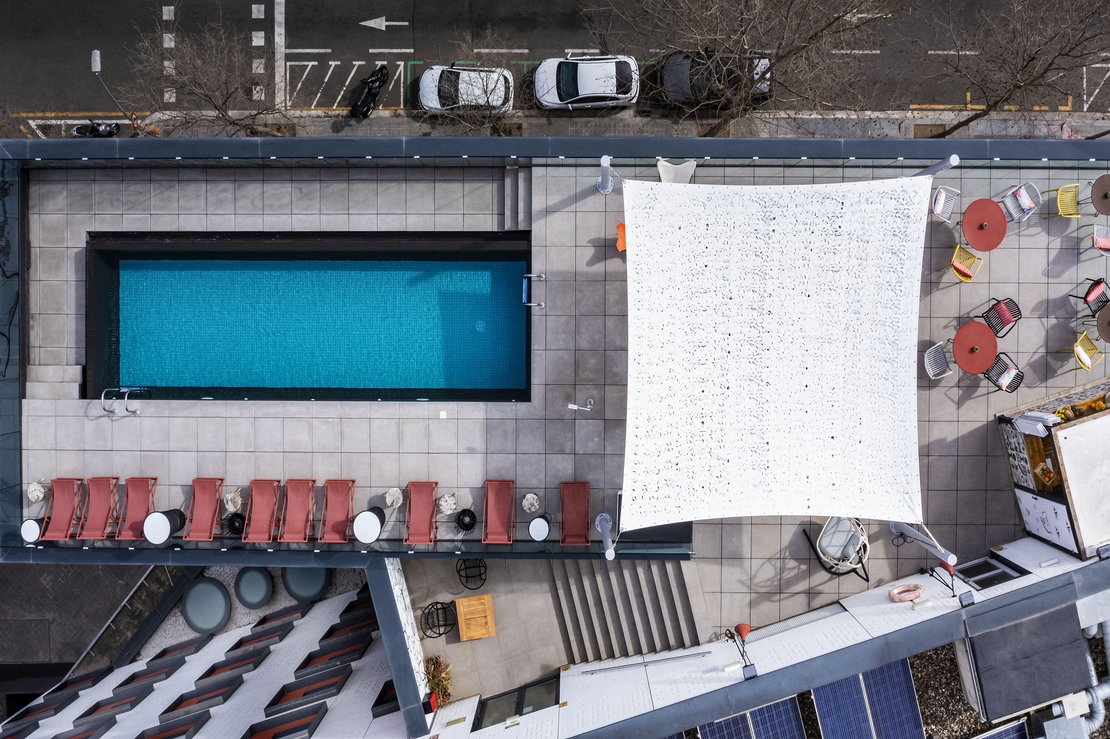 An aerial view of a rooftop pool area with a swimming pool, sun loungers, and outdoor seating.