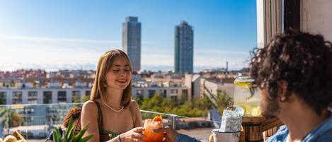 A person holding a drink at a bar with a city view in the background.