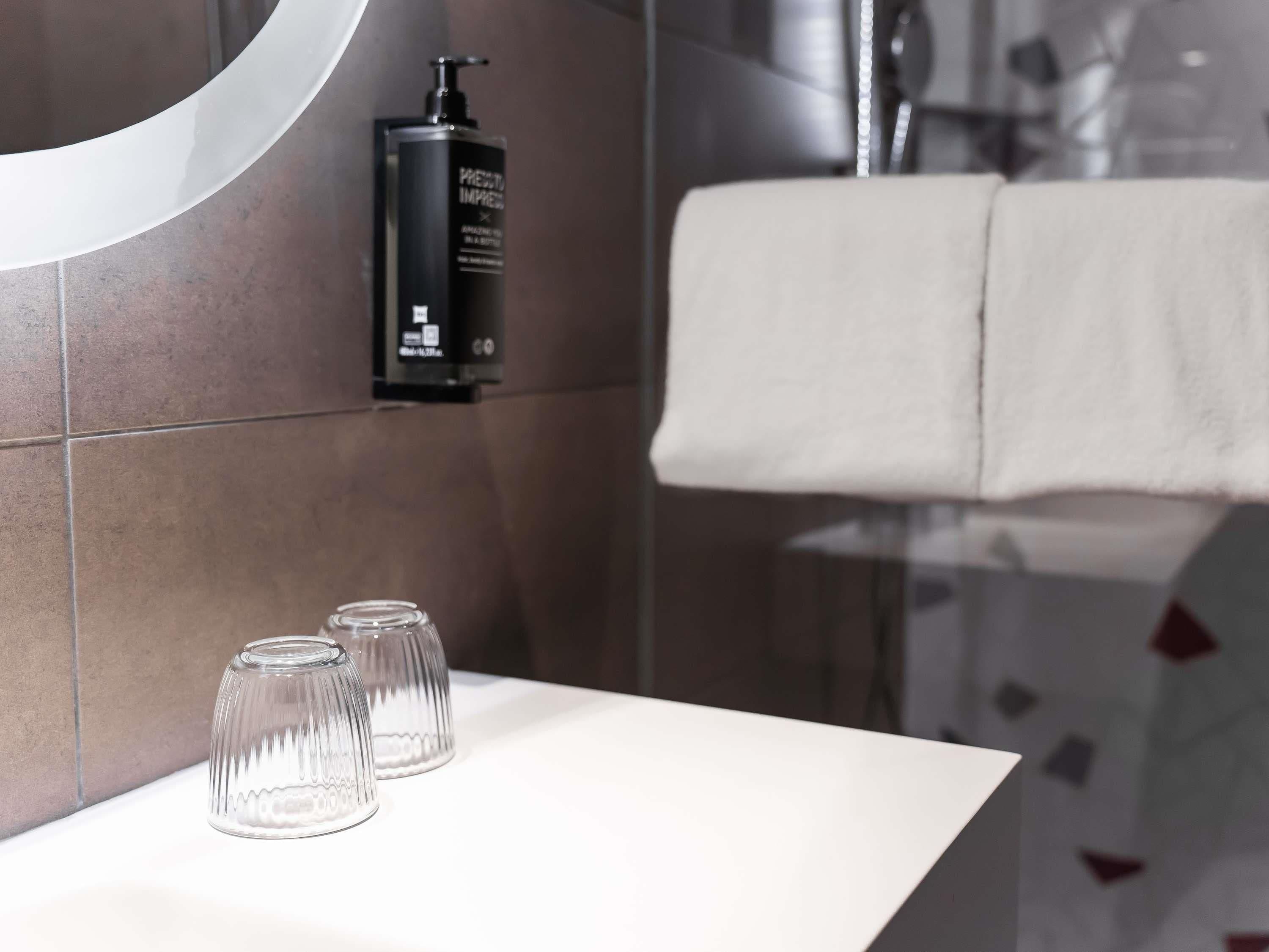 A bathroom with a white sink, a black bottle of shampoo, and two clear glass bottles.
