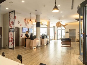A modern hotel lobby with a reception desk, wooden flooring, and a large decorative wall. - ibis Styles Barcelona City Bogatell (Barcelona)