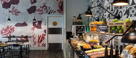 En morgenmadsbuffet med forskellige retter, en kaffemaskine og en væg med abstrakte mønstre.