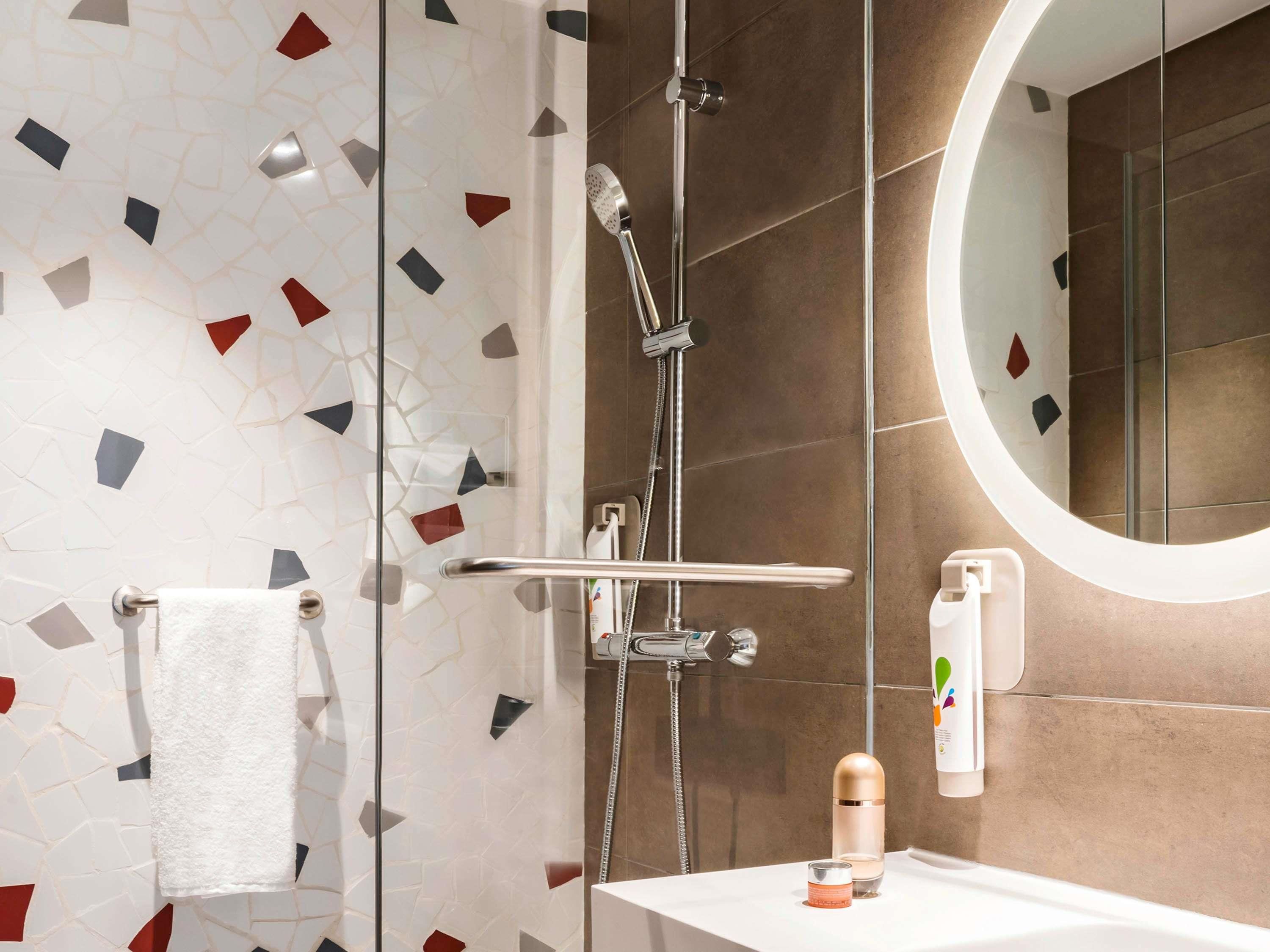 A modern bathroom with a shower, a round mirror, and a sink with toiletries.