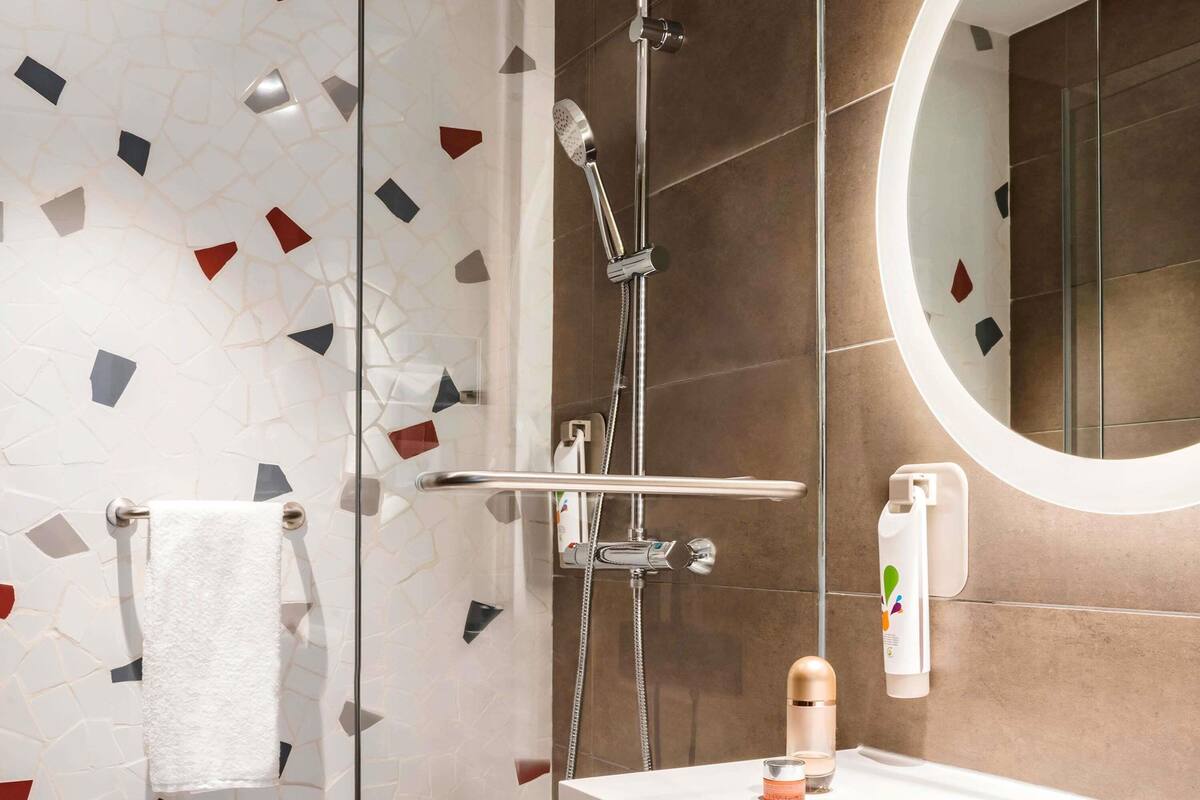 A modern bathroom with a shower, a round mirror, and a sink with toiletries.
