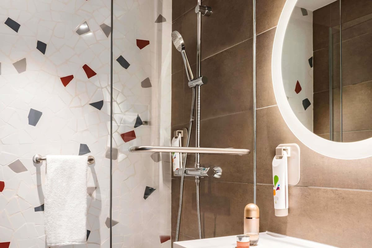 Une salle de bain moderne avec une douche, un miroir rond et un lavabo équipé de produits de toilette.