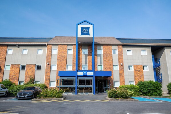 A hotel with a prominent 'ibis budget' sign, a brick facade, and a parking area with a blue parking space. - ibis budget Marne la Vallee Chelles (Chelles)