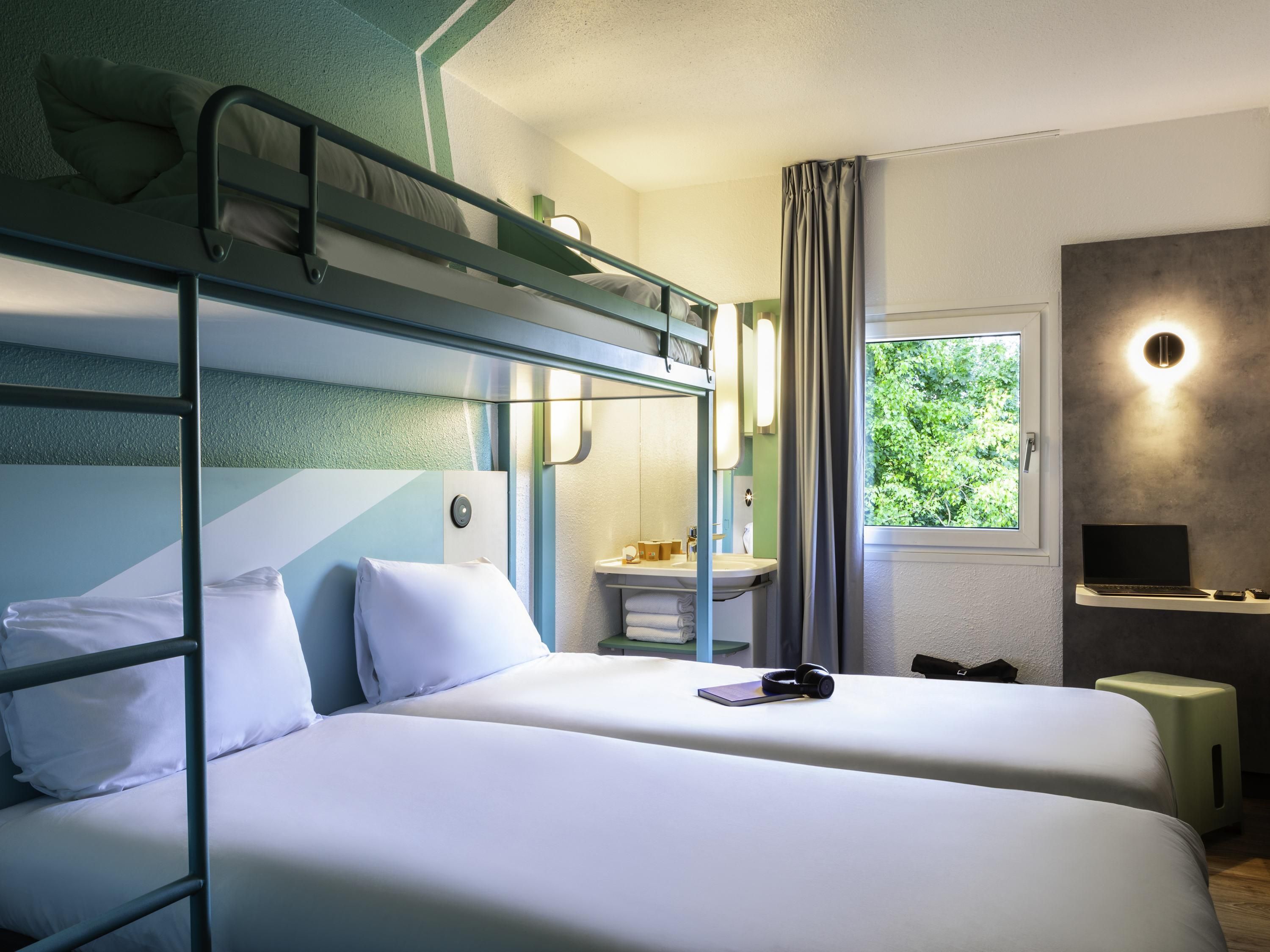 Une chambre avec un lit superposé, un bureau, un miroir et une fenêtre donnant sur un paysage verdoyant.