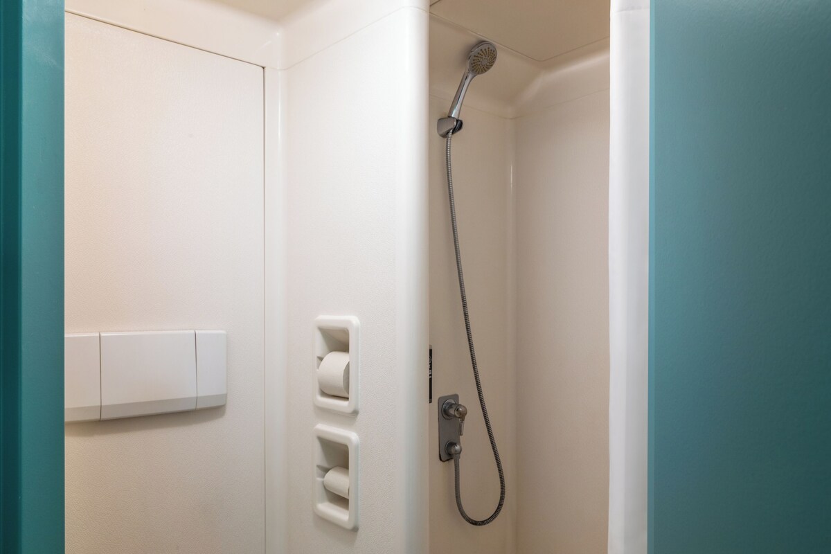 Un baño con ducha, dispensador de papel higiénico y un interruptor de luz.
