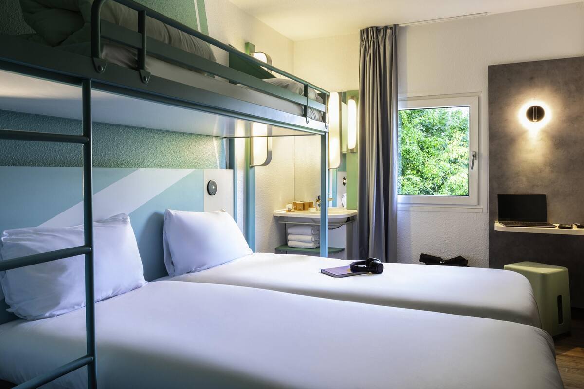 Une chambre avec un lit superposé, un bureau, un miroir et une fenêtre donnant sur un paysage verdoyant.