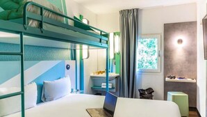 A bunk bed room with a laptop on the lower bed, a desk with a chair, a window with curtains, and a small stool.