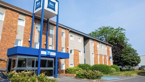 Un hôtel avec une enseigne bleue et blanche, une façade en briques et un espace de stationnement.
