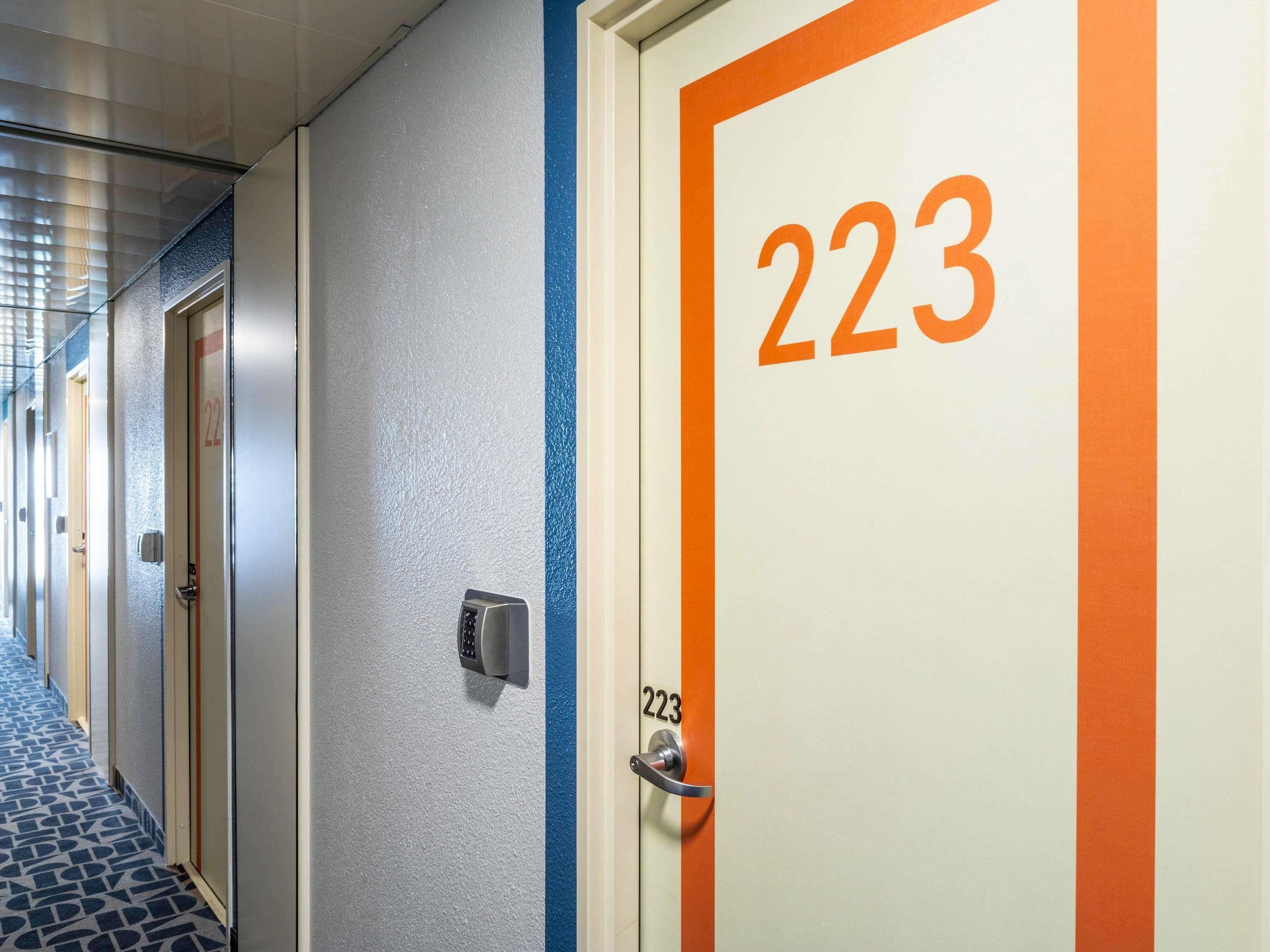 Un couloir d’hôtel avec des portes numérotées, à commencer par la porte 223, une moquette bleue et un clavier de sécurité.