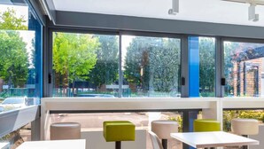 Un espace extérieur moderne aménagé avec des tables et des chaises, de grandes fenêtres offrant une vue sur les arbres et la rue.