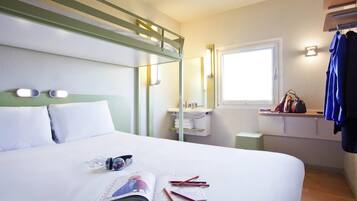 Habitación de hotel con literas, una mesita de noche con una revista y lápices, una ventana con vistas y un perchero.