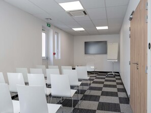 A conference room with white chairs, a large screen, and a checkered floor. - ibis budget Lyon Caluire Cite Internationale (Caluire-et-Cuire)