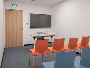 A conference room with a large screen, a wooden door, and orange and blue chairs. - ibis budget Lyon Caluire Cite Internationale (Caluire-et-Cuire)