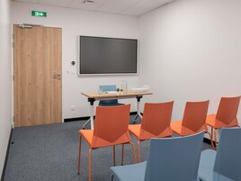 Una sala de conferencias con una pantalla grande, una puerta de madera y sillas anaranjadas y azules.