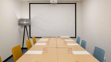 A conference room with a long table, chairs, a projector screen, and a floor lamp.