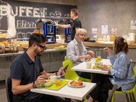 Un desayuno con gente comiendo, un área de bufé al fondo y una máquina de café.