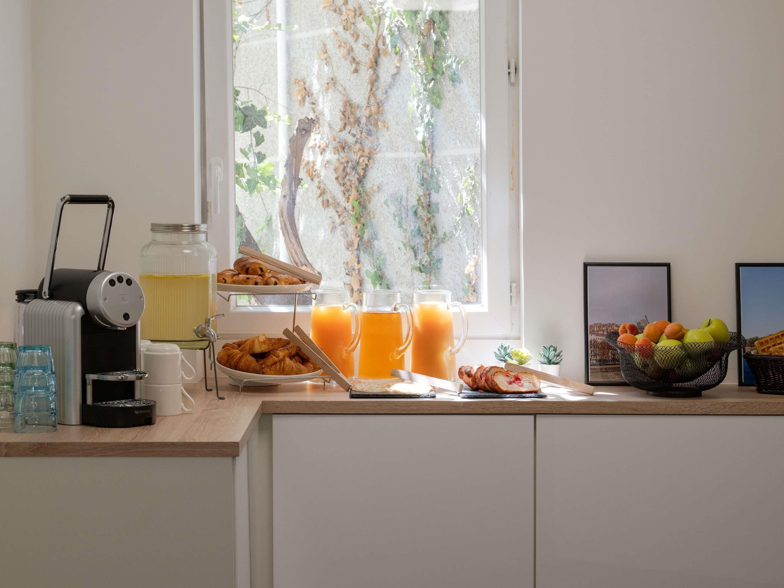 A breakfast setup with croissants, juice, and a fruit bowl on a kitchen counter.