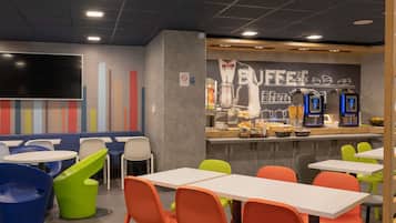Een café met tafels en stoelen, een balie met koffiemachines en een muur met een koffie-gerelateerde muurschildering.