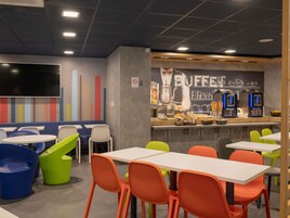 Un café con mesas y sillas, una barra con máquinas de café y una pared decorada con un mural de temática cafetera.