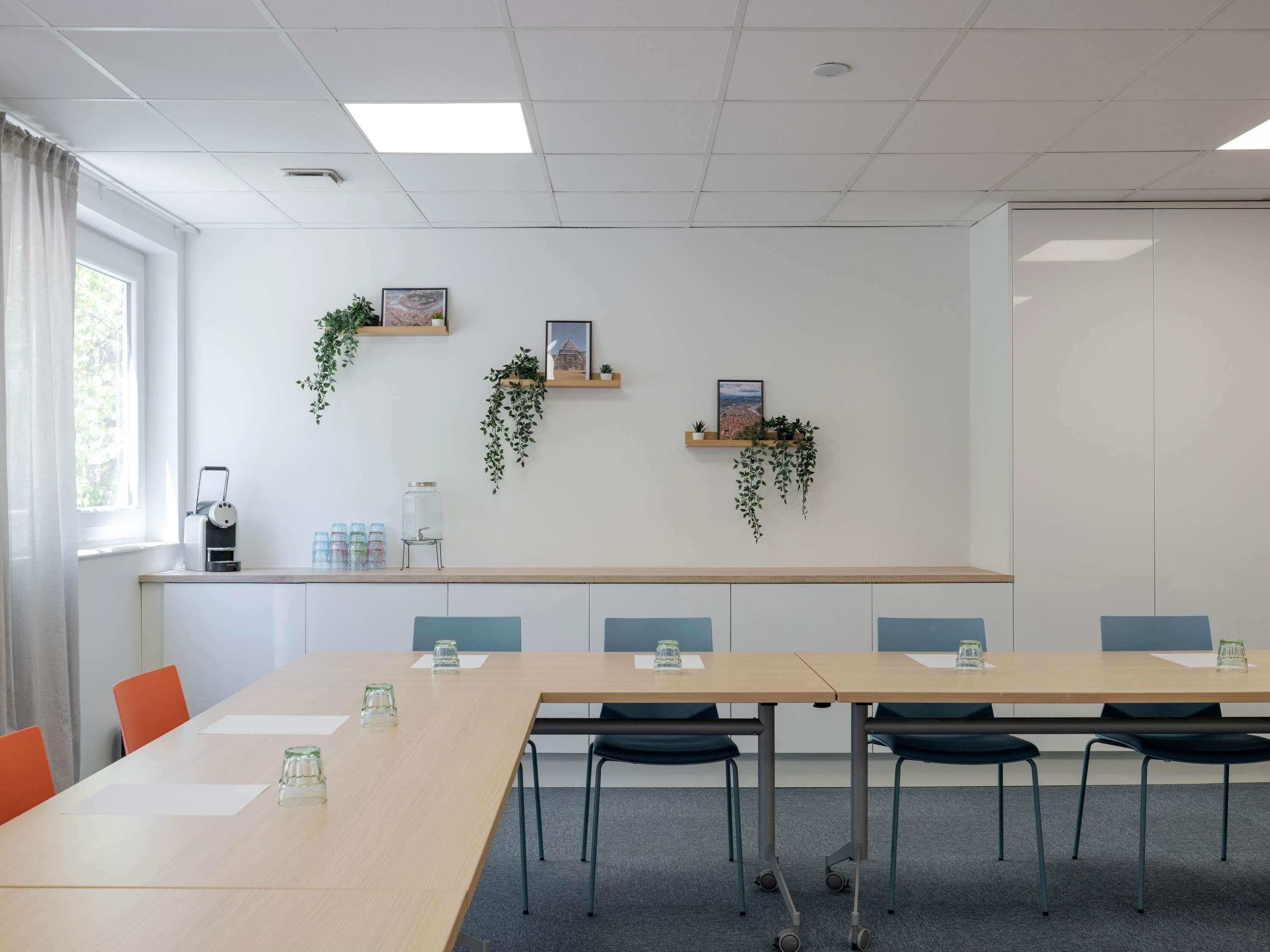 A conference room with a long table, chairs, a coffee machine, and decorative plants.