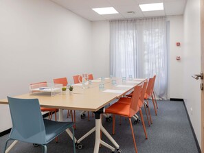 Un salón de conferencias con una mesa larga, sillas, una jarra de agua y una planta pequeña.