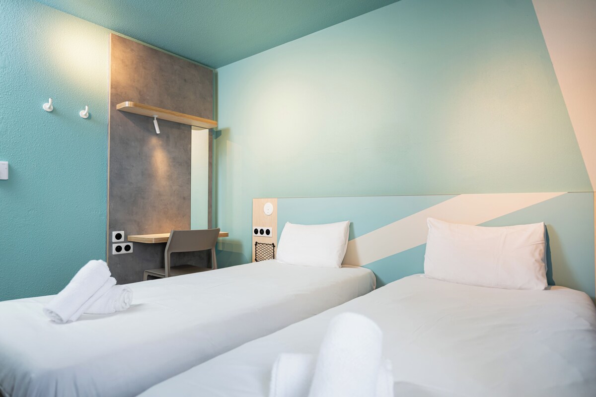 A hotel room with two beds, a desk, and a chair.
