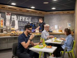 A breakfast area with a coffee machine, seating, and a menu board. - ibis budget Lyon Caluire Cite Internationale (Caluire-et-Cuire)