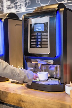 A coffee machine with a digital interface and a cup placed underneath. - ibis budget Lyon Caluire Cite Internationale (Caluire-et-Cuire)