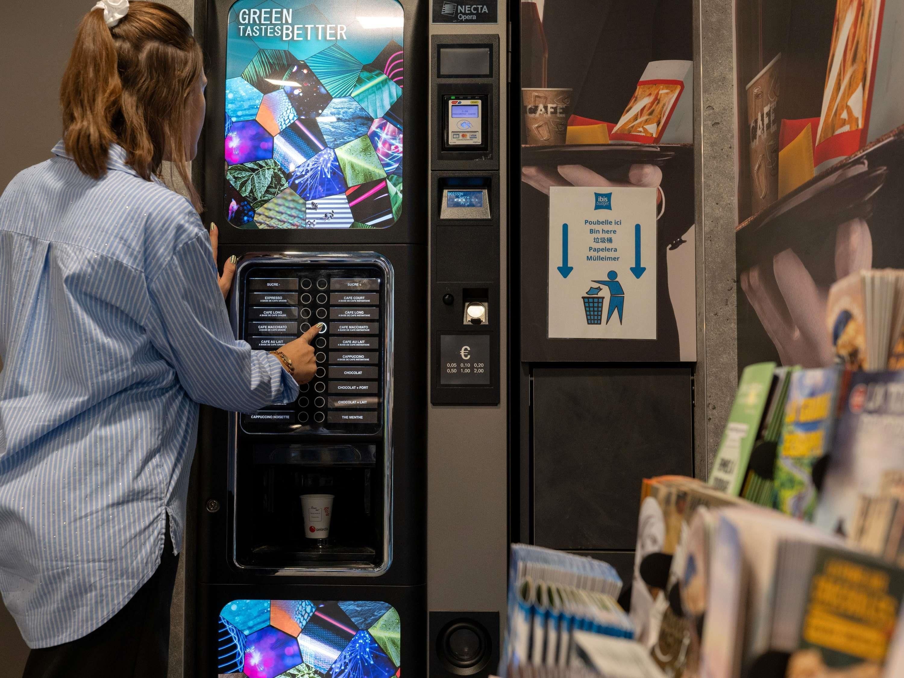 A person interacting with a coffee vending machine with a digital display and a payment terminal.