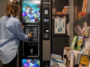 A person interacting with a coffee vending machine with a digital display and a payment terminal. - ibis budget Lyon Caluire Cite Internationale (Caluire-et-Cuire)