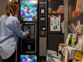 Una persona utilizando una máquina expendedora de café con pantalla digital y terminal de pago.