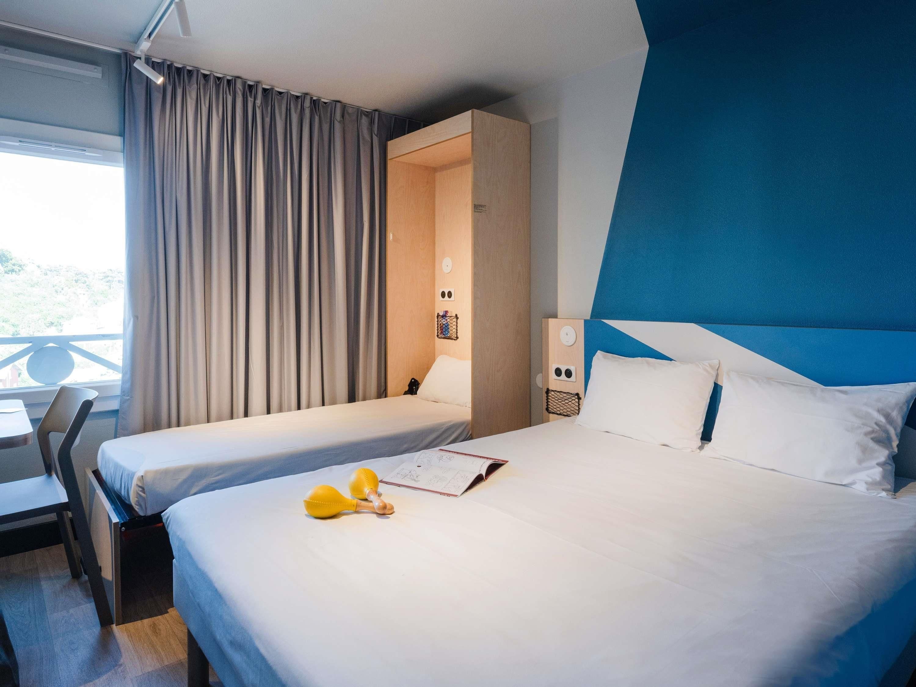 A hotel room with two beds, a desk, and a view of the outdoors.