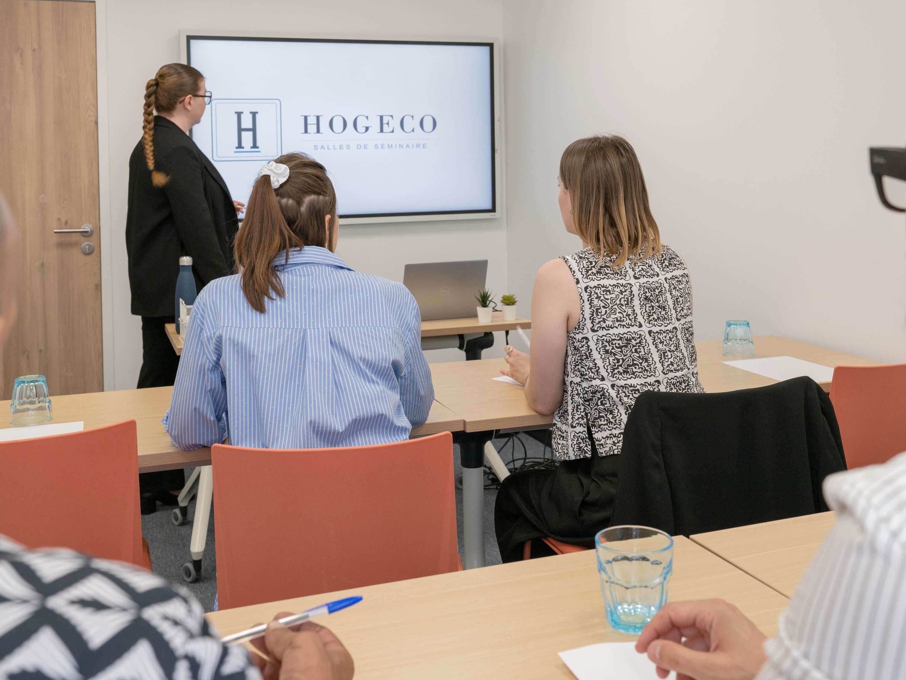 Un salón de conferencias con una pantalla de presentación que muestra 'HOGEOCO SALLES DE SEMINAIRE'.