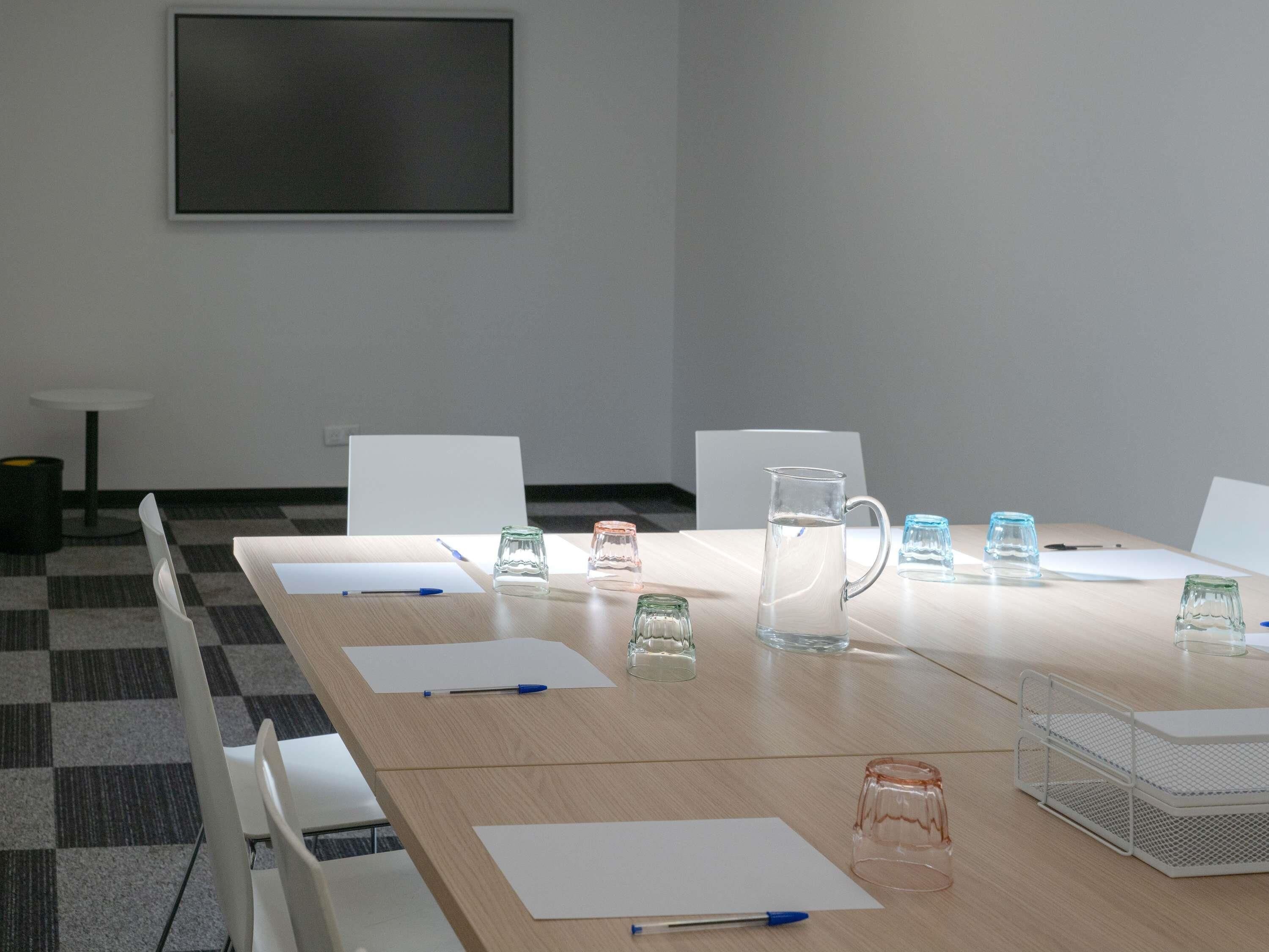 A conference room with a long table, chairs, a whiteboard, and various items like glasses and a water pitcher.